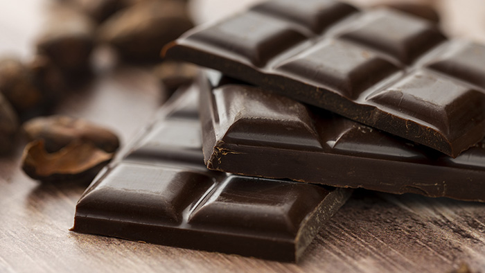 Close-up of stacked dark chocolate bars on a wooden surface with cocoa beans in the background.