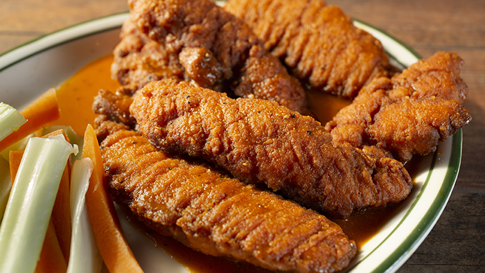 A plate of buffalo chicken tenders served with celery and carrot sticks on the side.